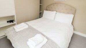 A neatly made bed with white linens and two folded towels on a gray carpet. - Swainby Cottage (Northallerton)