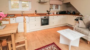 A modern kitchen with white cabinets, a wooden countertop, a built-in oven, and a dining area with a wooden table and chairs. - Swainby Cottage (Northallerton)