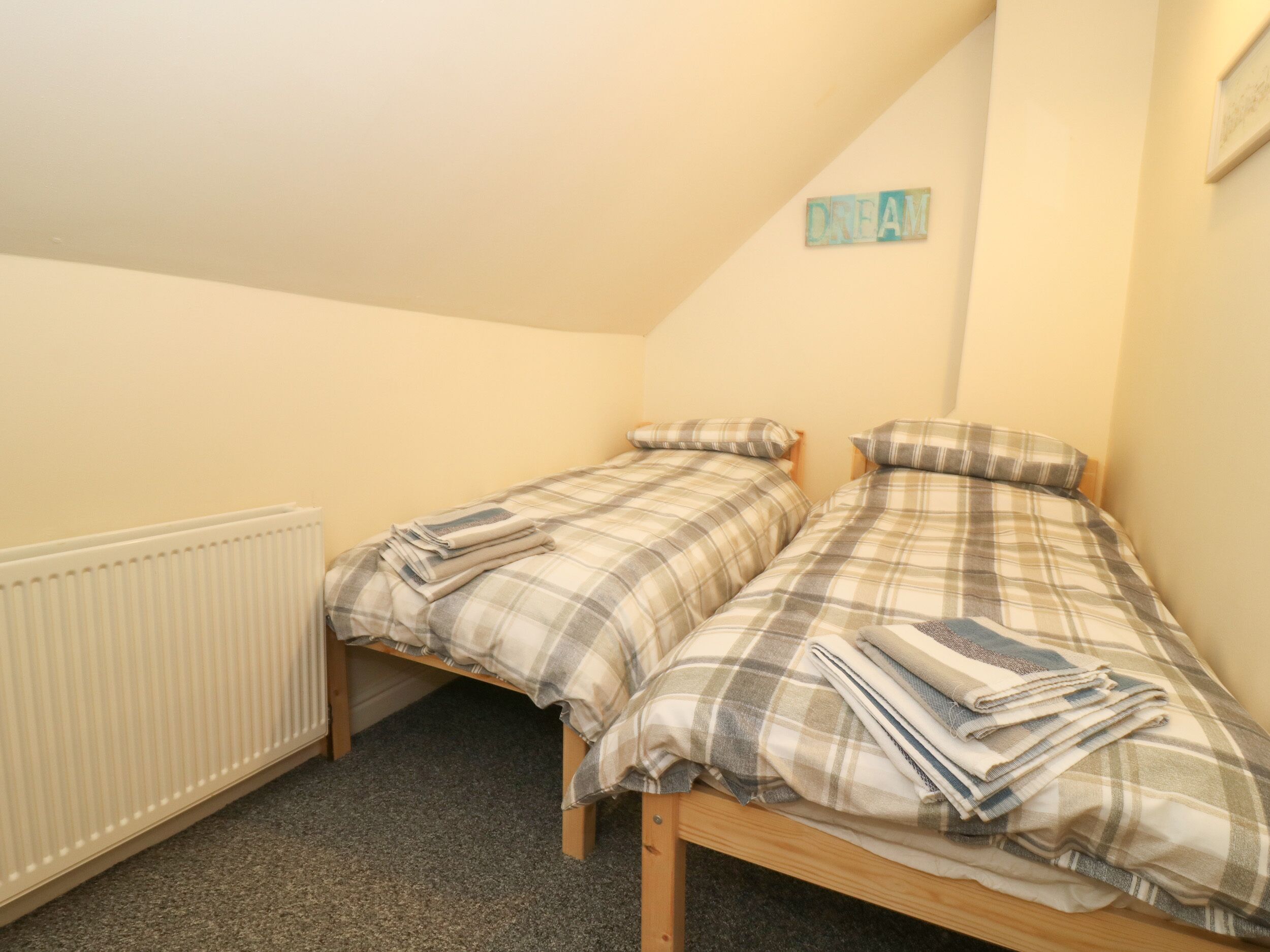 A small, cozy bedroom with two single beds, a radiator, and a 'DREAM' sign on the wall.