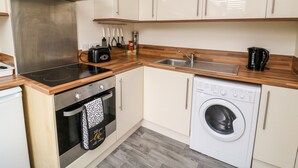A compact kitchen with a built-in oven, a microwave, a stove, a sink, and a washing machine. - The Pebbles (Hornsea)