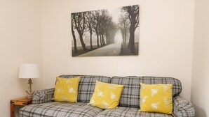 A plaid sofa with three yellow pillows, a lamp, and a framed picture of a tree-lined path on the wall. - The Pebbles (Hornsea)