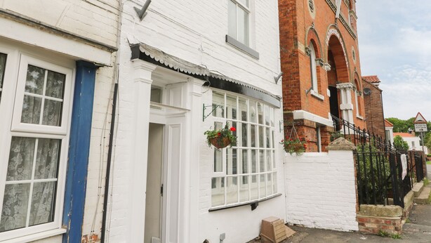 A row of white brick houses with a red brick building in the background. - The Pebbles (Hornsea)