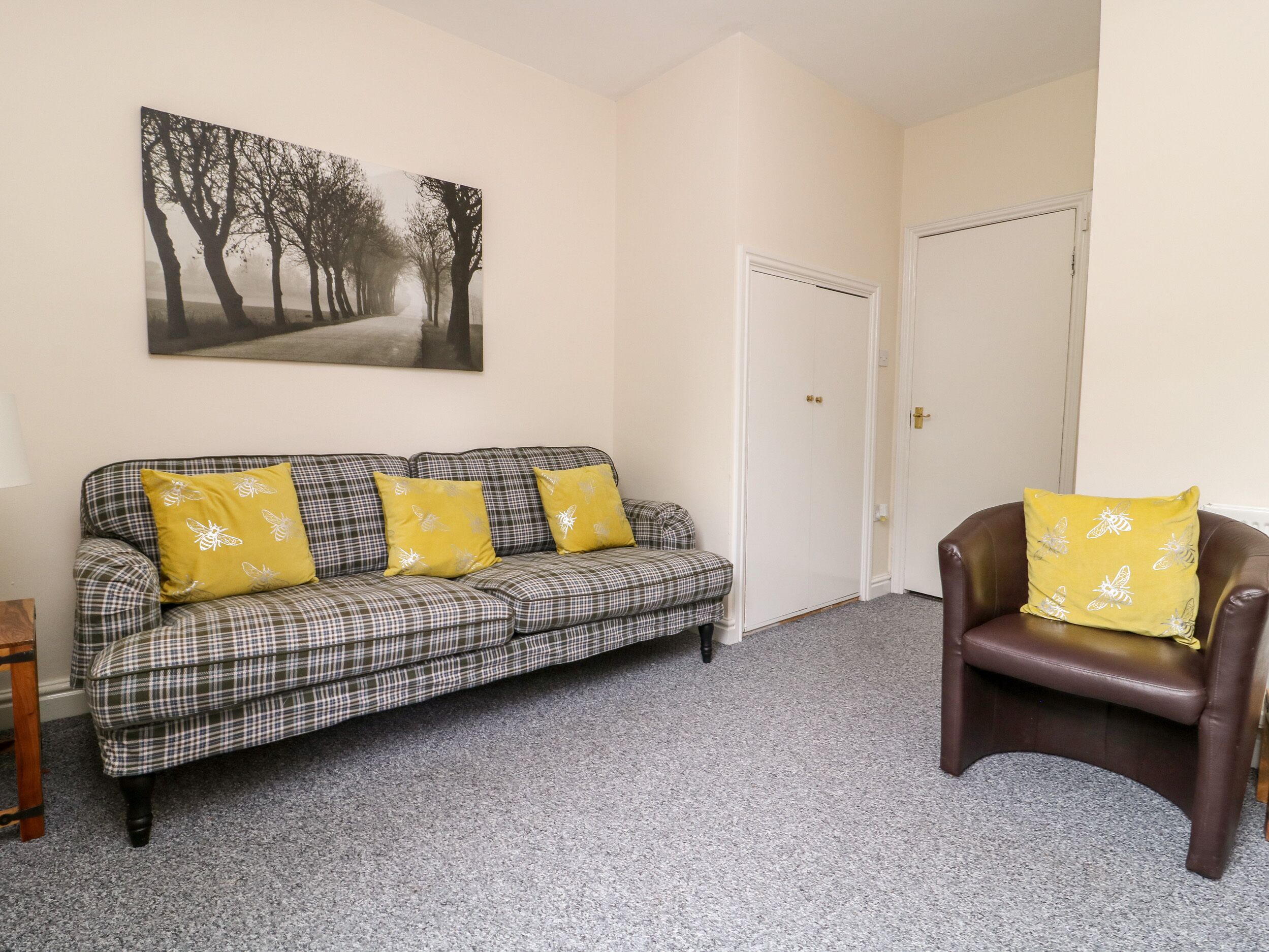 A living room with a plaid sofa, a brown leather chair, and a painting of trees.