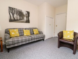 A living room with a plaid sofa, a brown leather chair, and a painting of trees.