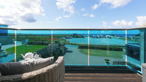A balcony with a view of a river and a bridge, a grassy area, and a modern building in the background. - Sandbanks (Penzance)