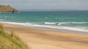 A beach with a rocky cliff and ocean waves. - Sandbanks (Penzance)