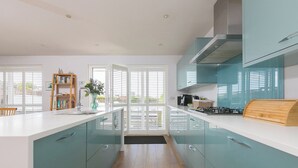 A modern kitchen with teal cabinetry, a white countertop, and a central island. - Sandbanks (Penzance)
