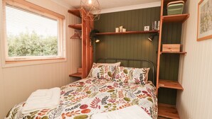 A bedroom with a bed, a window with blinds, a wooden shelf, and a hanging light fixture. - 3 Valley View Lodges (York)