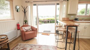 A modern kitchen with a wooden countertop, bar stools, a pink armchair, and a large rug. - 3 Valley View Lodges (York)