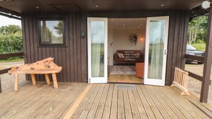 A wooden deck with a bench and a door leading to an interior space with a sofa and a wall-mounted light fixture. - 3 Valley View Lodges (York)
