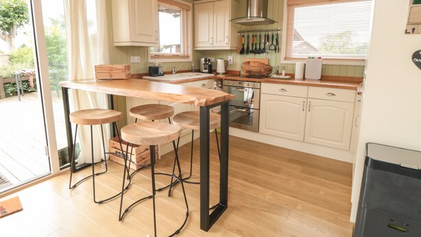 A kitchen with a central island, bar stools, a stove, and a large window. - 3 Valley View Lodges (York)