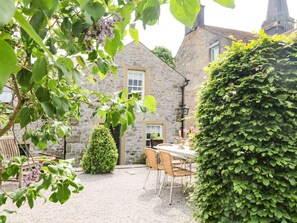 A stone building with a gravel patio, a table with chairs, and a hedge. - Church Cottage (Bakewell)