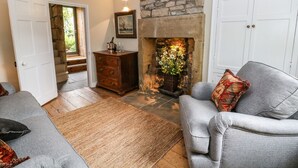Ein gemütliches Wohnzimmer mit Kamin aus Stein, grauen Sofas, einem Holzkasten und einer Tür zu einer Treppe.