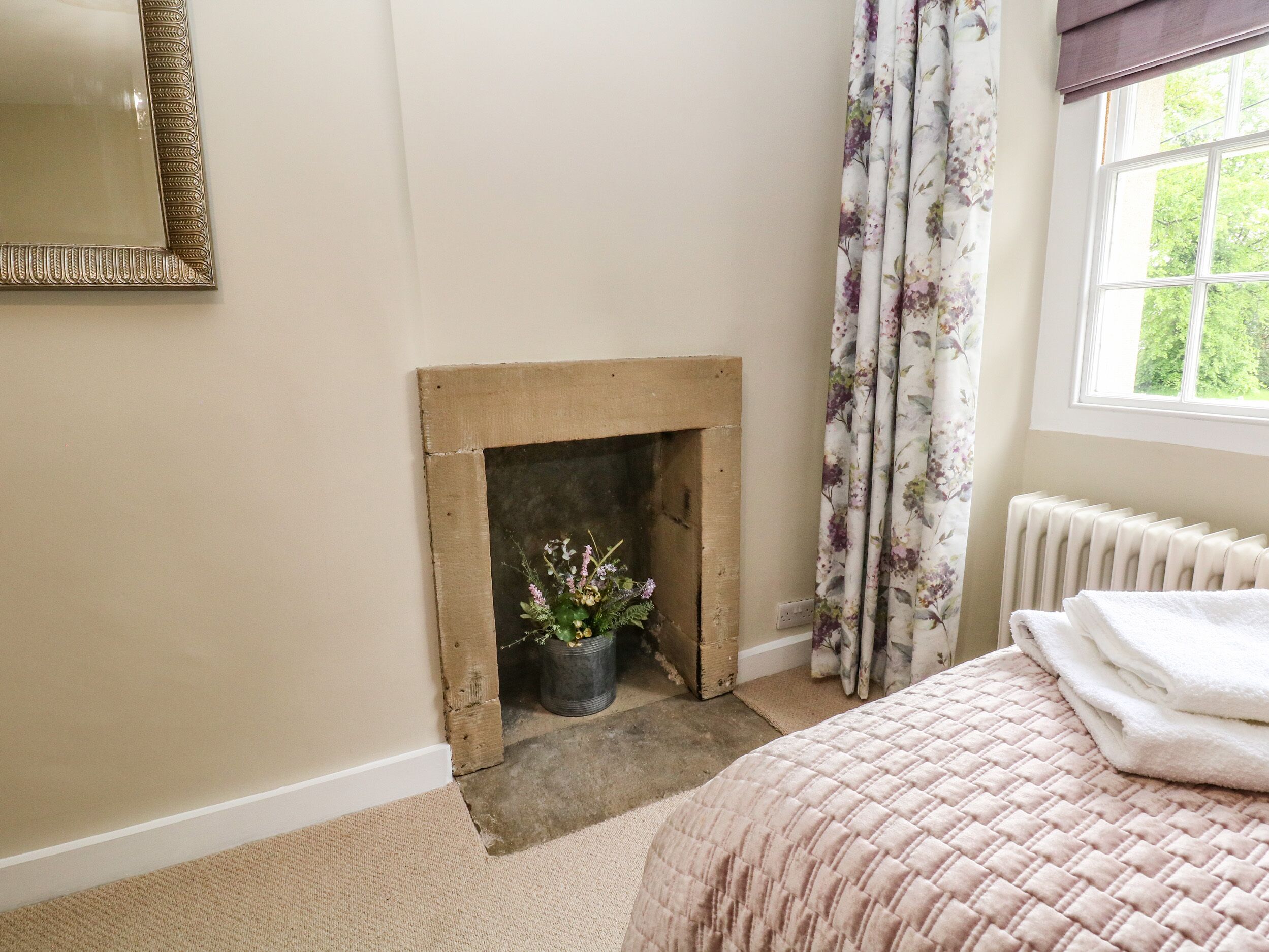 A bedroom with a fireplace, a window with curtains, a radiator, and a bed with a quilt.
