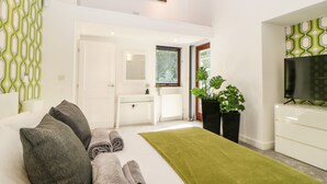 A modern bedroom with a bed, a desk, a mirror, a TV, and a green plant. - Iroko (Torpoint)