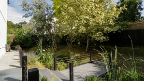 A wooden deck with a metal railing, surrounded by lush greenery and trees. - Iroko (Torpoint)