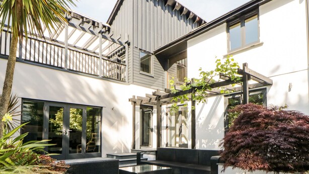 A modern two-story house with a patio, outdoor seating, and a pergola. - Iroko (Torpoint)
