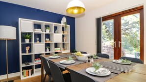 A dining area with a wooden table set for four, surrounded by chairs. A white bookshelf with various decorative items is to the left. - Iroko (Torpoint)