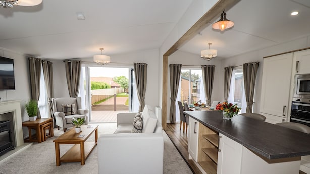 A modern living room with a sofa, coffee table, and TV. There is a kitchen area with a counter and cabinets. - Bramblewick (Saltburn-by-the-Sea)