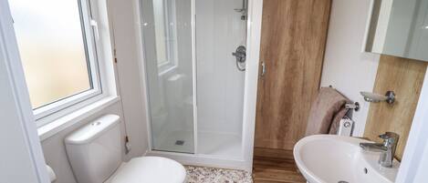 A bathroom with a toilet, shower, sink, and a window.
