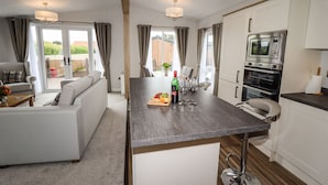 A modern kitchen with a central island, white cabinetry, and a dining area with a sofa and table. - Bramblewick (Saltburn-by-the-Sea)