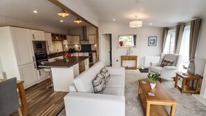A modern kitchen with white cabinets, a central island, and a dining area with a sofa and wooden table. - Bramblewick (Saltburn-by-the-Sea)