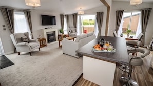 A modern living room with a fireplace, a sofa, a dining area with a bar, and a TV mounted on the wall. - Bramblewick (Saltburn-by-the-Sea)