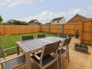 A patio area with a table and chairs, surrounded by a wooden fence and a grassy lawn. - Turnstone (Barnstaple)