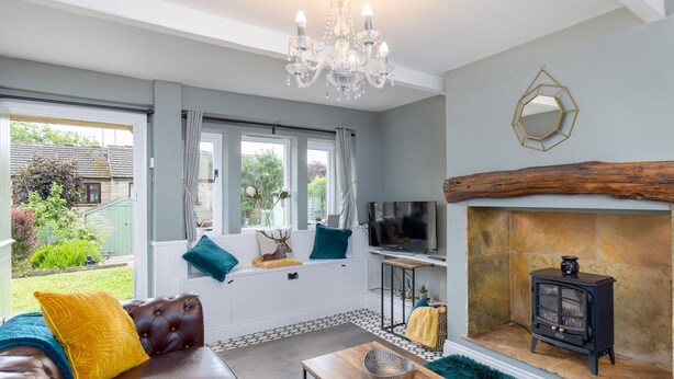 A living room with a sofa, TV, fireplace, and a view of the garden. - Mischa Cottage (Bradford)