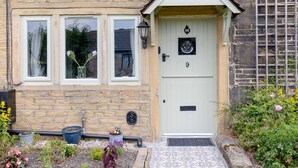 A house with a stone facade, a white door with the number 9, and a small porch with a light fixture. - Mischa Cottage (Bradford)