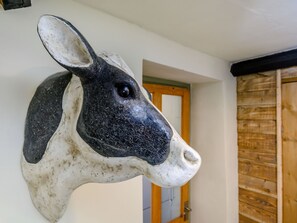 A mounted cow head sculpture in a room with a wooden door and a white wall. - Hoglets (Minehead)