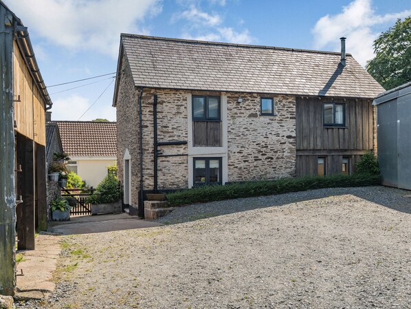 A two-story stone house with a sloped roof, a gravel driveway, and a wooden fence. - Hoglets (Minehead)