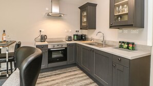 Une cuisine moderne avec des meubles de rangement de couleur sombre, un four encastré, un four à micro-ondes, une bouilloire et un évier.