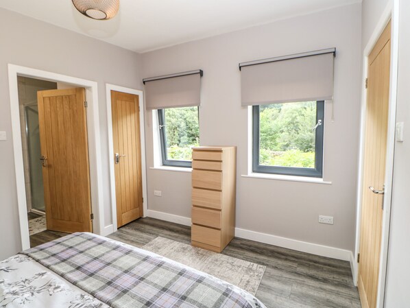 A bedroom with a bed, two windows, a wardrobe, and a door.