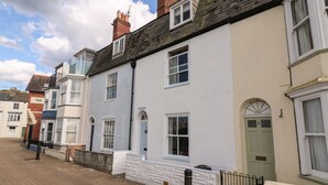 A row of terraced houses with white and light blue exteriors, a brick chimney, and a clear blue sky. - Harbourside Cottage (Weymouth)
