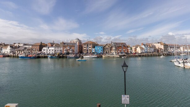 A harbor with boats docked, a lamppost, and buildings along the waterfront. - Harbourside Cottage (Weymouth)