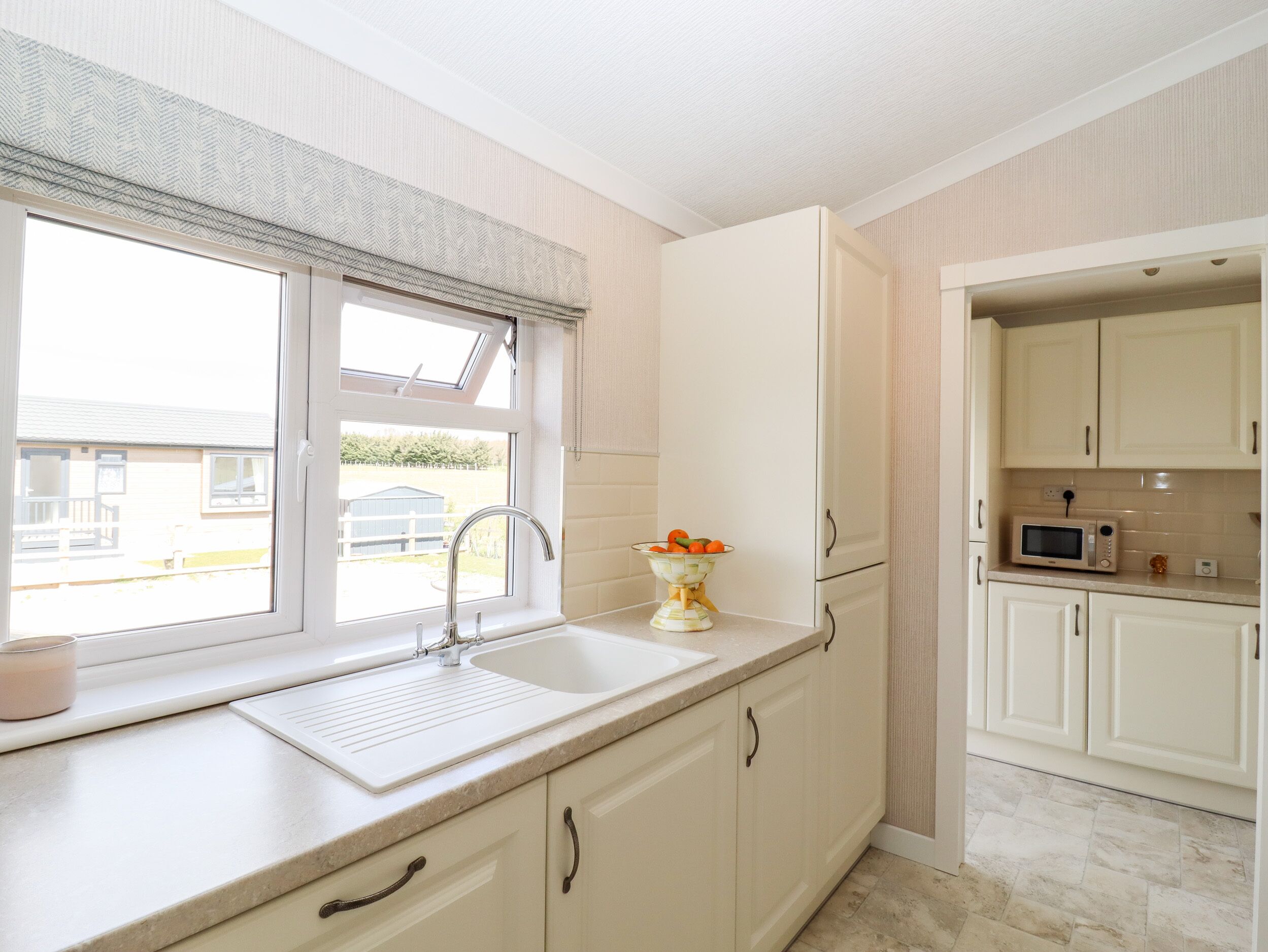 A kitchen with a window, sink, cabinets, and a microwave.