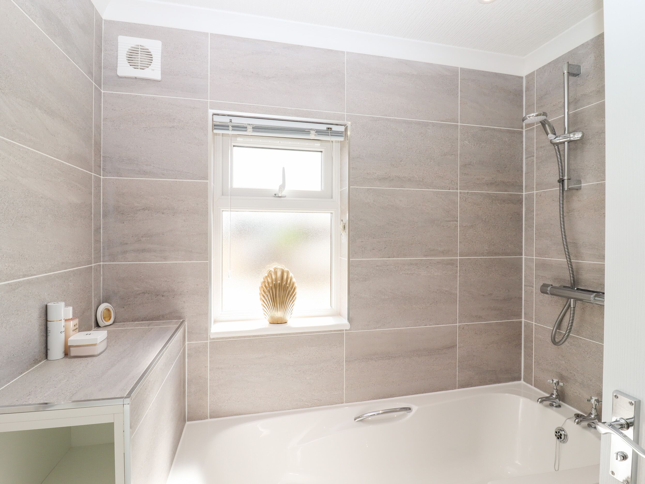 A modern bathroom with a bathtub, shower, and a window with a decorative vase.