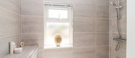 A modern bathroom with a bathtub, shower, and a window with a decorative vase.