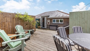 Une terrasse en bois avec des meubles d’extérieur, notamment des chaises et une table, et une maison en arrière-plan.