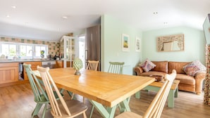 Une cuisine spacieuse avec une table et des chaises en bois, un coin repas avec un canapé et un salon avec un divan et un miroir.