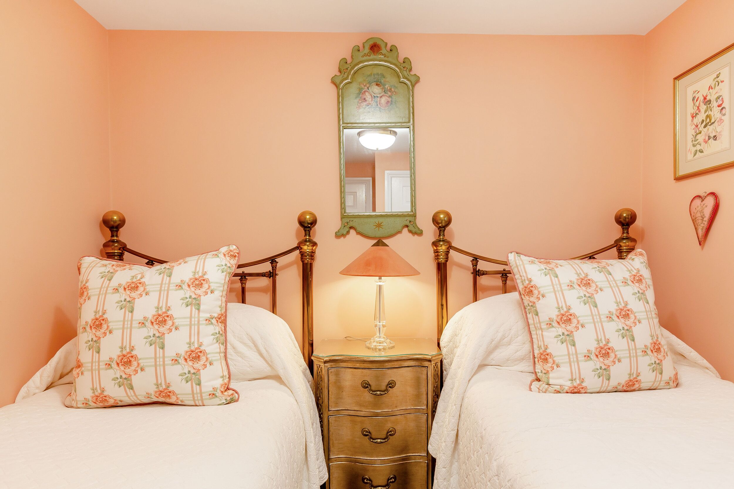 Quarto com duas camas, uma cômoda, um espelho e um abajur.