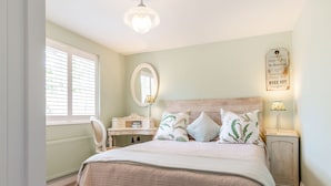 Une chambre à coucher comprenant un lit, une table de chevet, un miroir, une horloge murale et une fenêtre avec des stores.