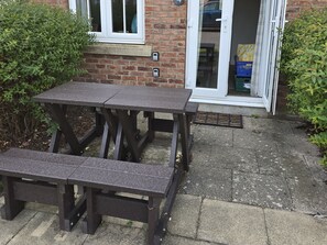 A wooden picnic table and bench outside a building with a brick facade and a glass door.