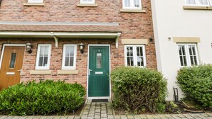 A two-story brick house with a green door, white-framed windows, and a small front garden. - Puffin Cottage (Filey)