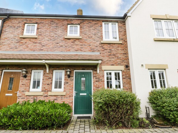 A two-story brick house with a green door, white-framed windows, and a small front garden.