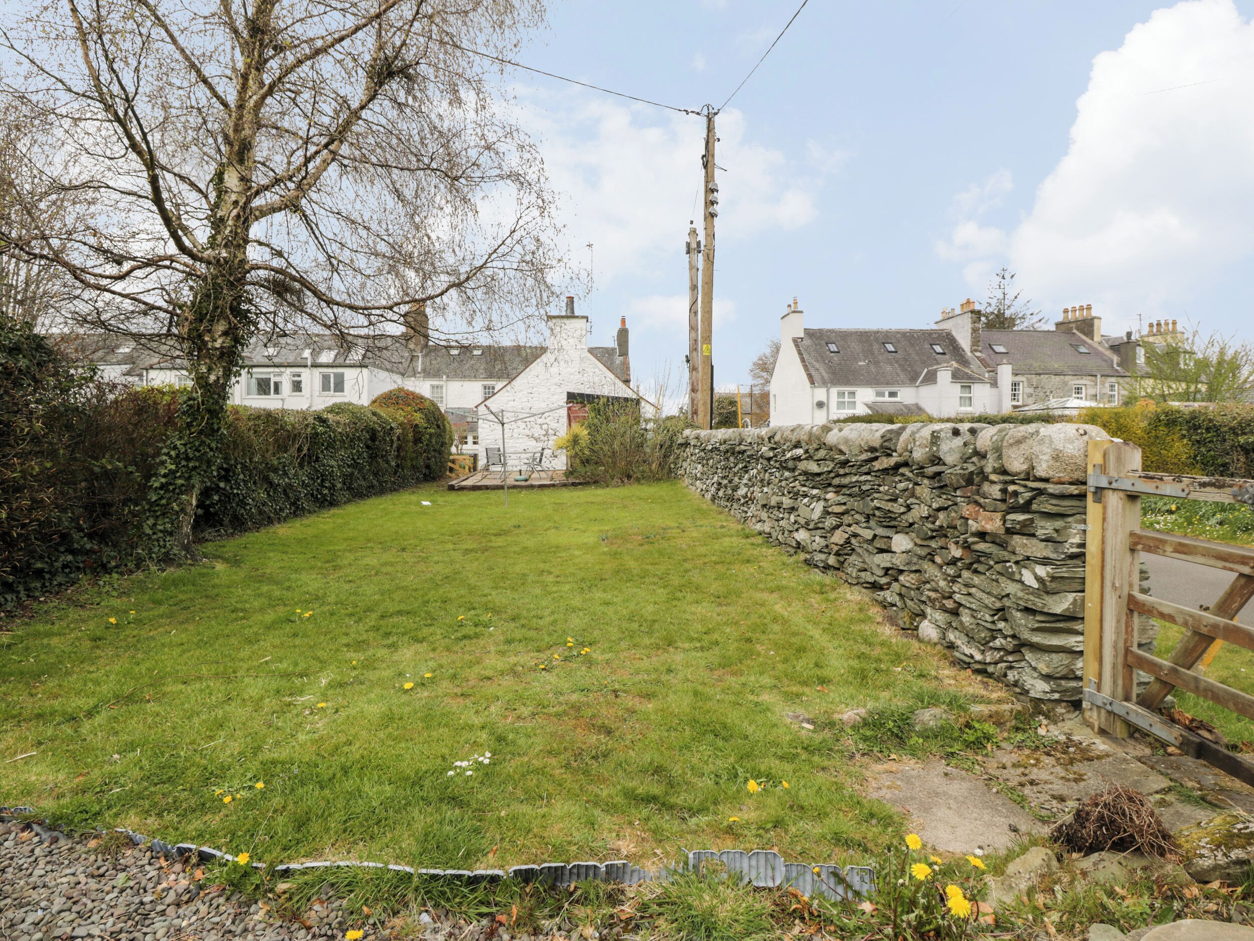 A stone wall, a wooden gate, and a grassy area with a small shed.