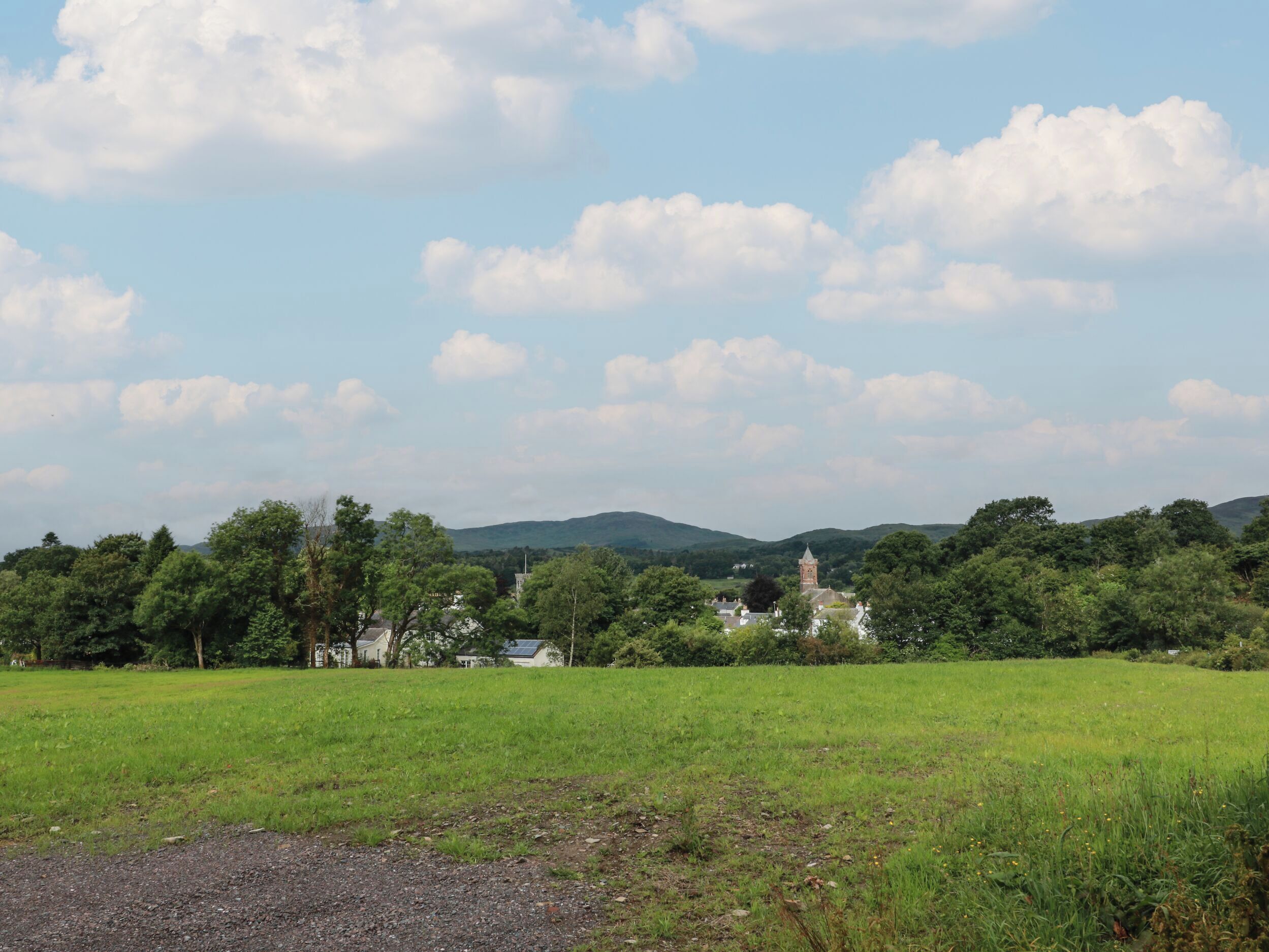 A rural landscape with a field, trees, and a distant building with a tower.