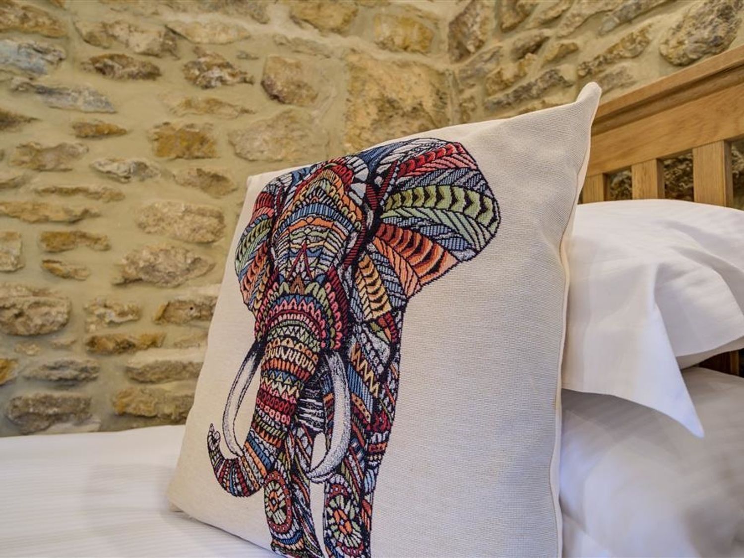 Un almohadón con un diseño de elefante colorido, sobre una cama con sábanas blancas.