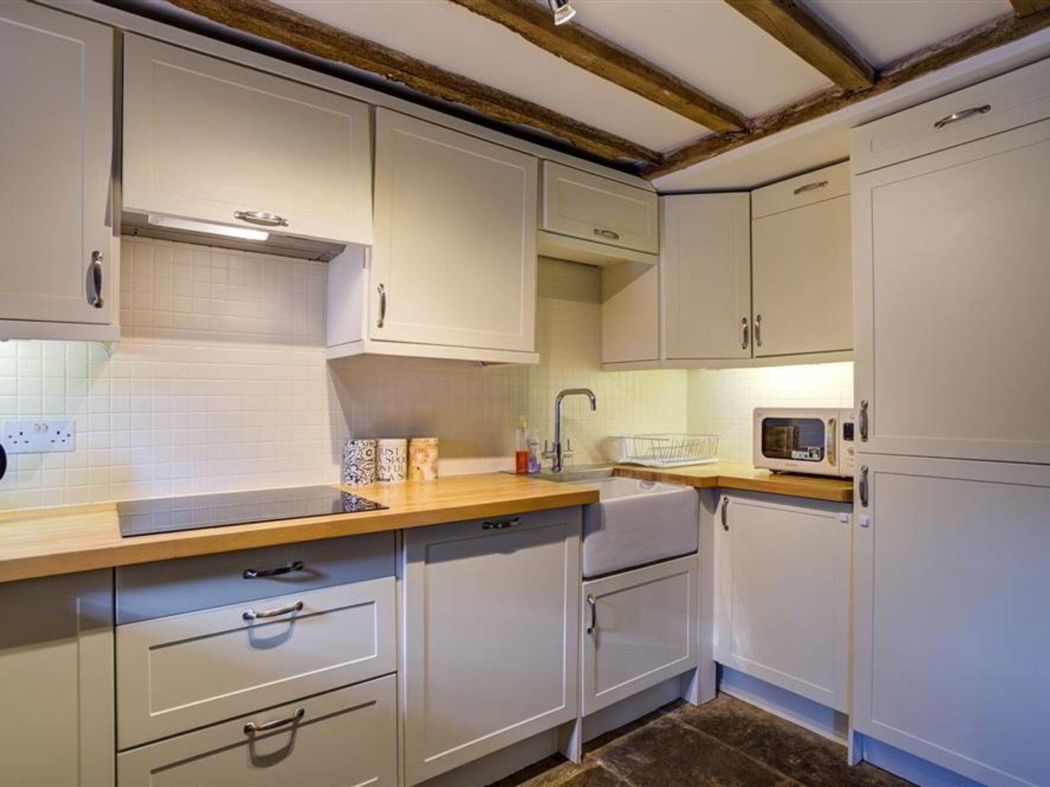 A kitchen with white cabinets, a wooden countertop, a microwave, and a sink.